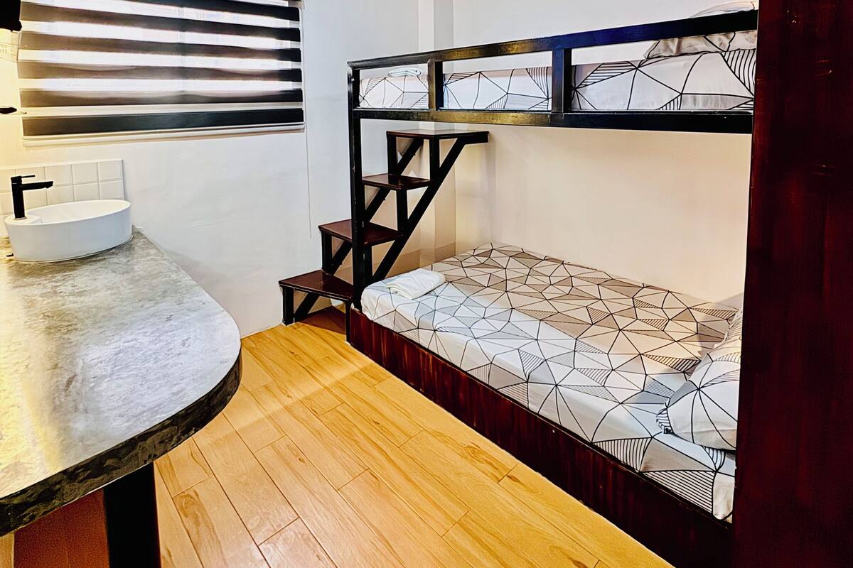 A compact room with a bunk bed, a round table with a sink, and a ceiling fan.