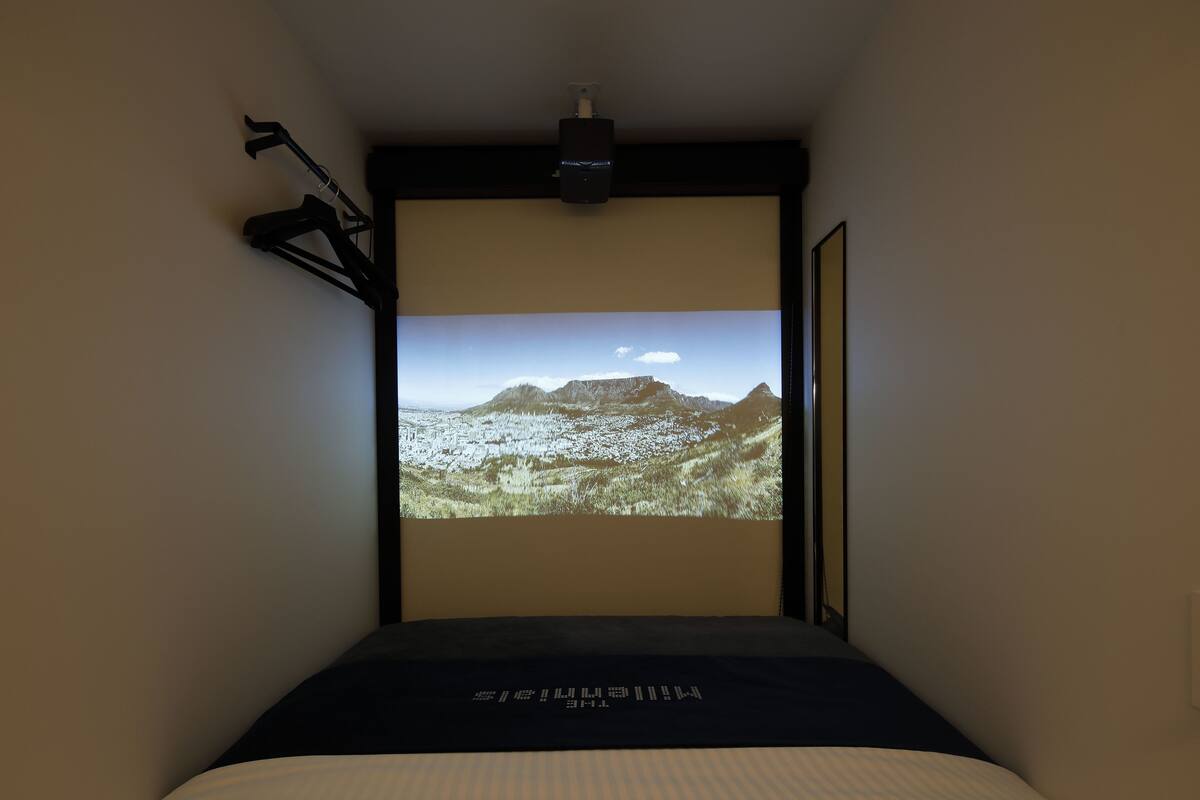 Une chambre à coucher avec un lit, un projecteur fixé au plafond et un écran diffusant une image de paysage.
