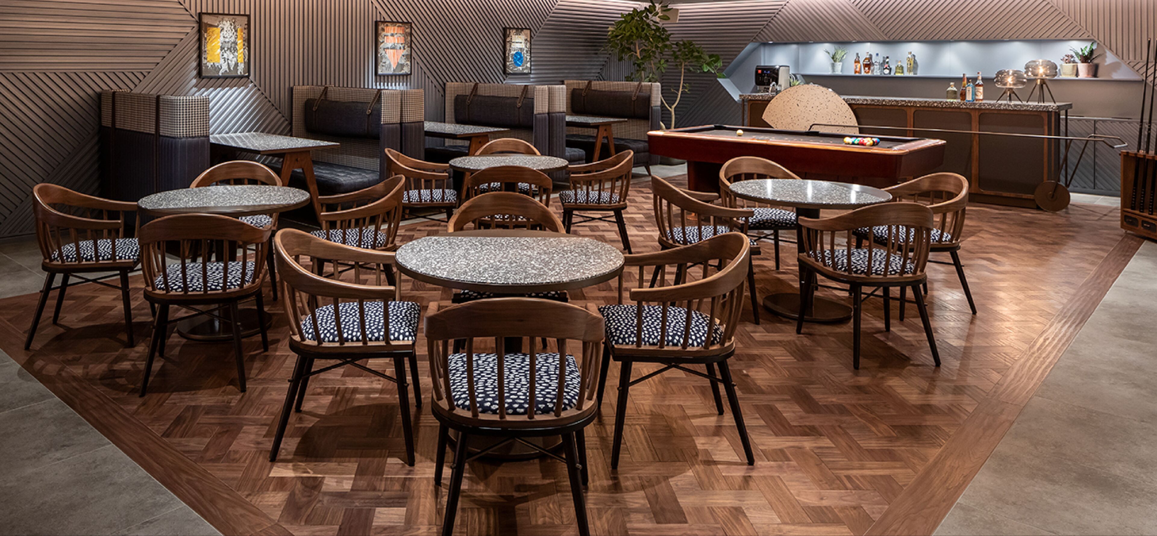 A restaurant with wooden flooring, round tables, and chairs with patterned cushions.