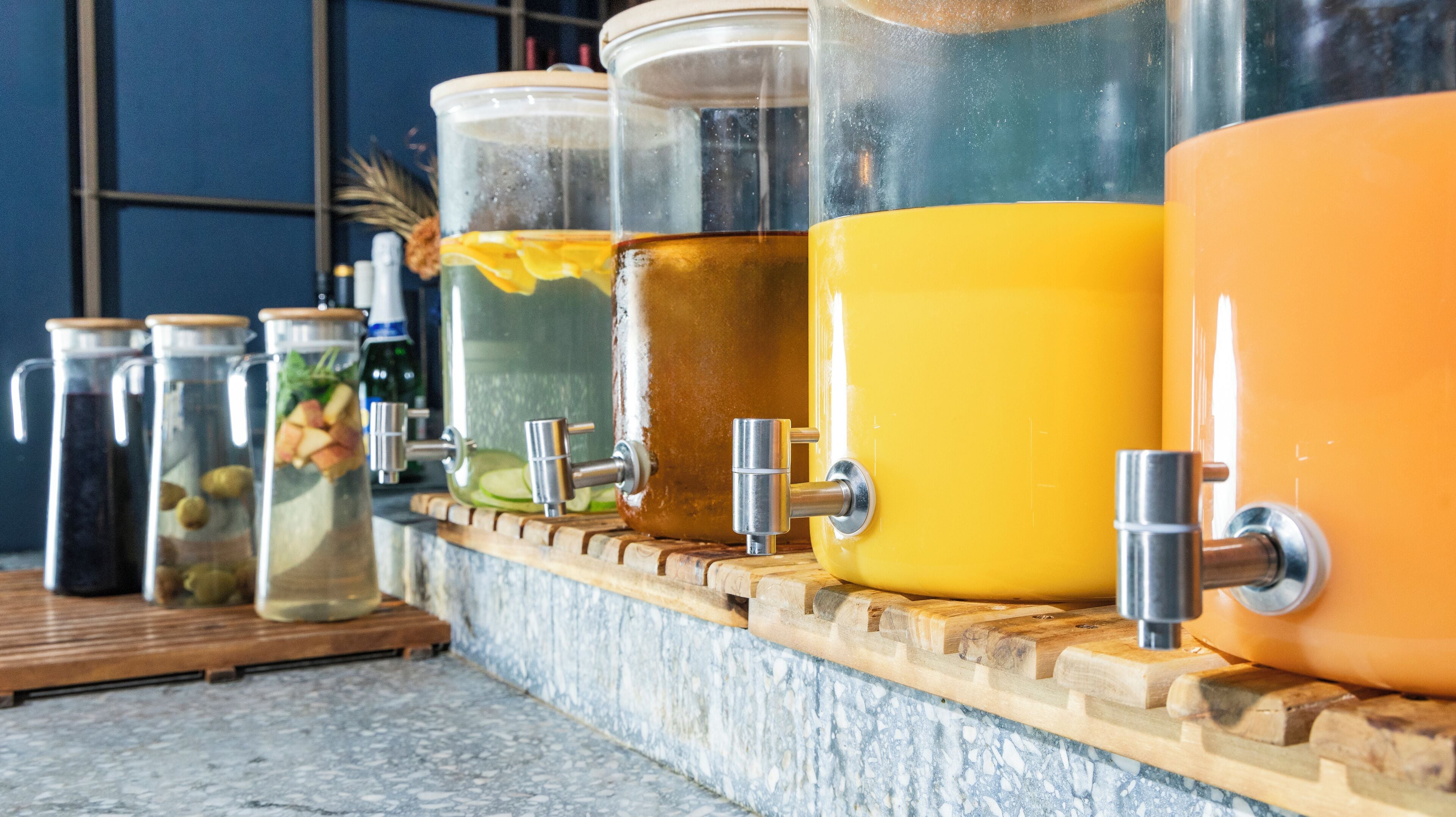 A row of large beverage dispensers on a wooden counter.