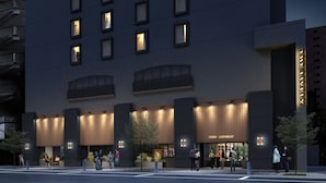 Een modern hotelgevel met verlichte borden, een begane grond ingang en een zichtbaar terras.
