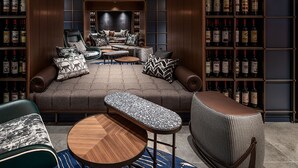 Een knus zithoekje met een bank, fauteuils en een salontafel, omringd door boekenkasten vol boeken en wijnflessen.
