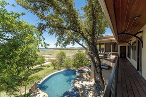 A pool area with a view of the landscape, a covered deck, and a building with large windows.