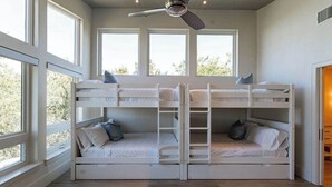 Una habitación con literas, ventilador de techo y ventanas amplias.