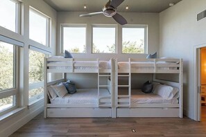 Una habitación con literas, ventilador de techo y ventanas amplias.