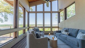 Un salón amplio con ventanas grandes, un sofá gris, un sillón gris y una mesa de centro.