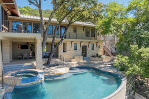 Une maison à deux étages avec une piscine, une façade en pierre et un balcon agrémenté de mobilier d’extérieur.