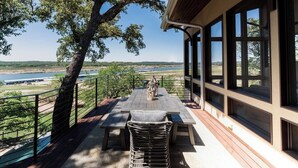 Un espacio de estar al aire libre techado con una mesa y sillas, con vistas a un cuerpo de agua y el paisaje.