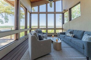 Un salon spacieux avec une grande fenêtre, un canapé gris, un fauteuil gris et une table basse.