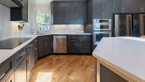 Cocina moderna con armarios oscuros, electrodomésticos de acero inoxidable y piso de madera.