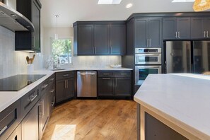 Cocina moderna con armarios oscuros, electrodomésticos de acero inoxidable y piso de madera.