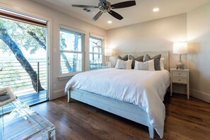 A bedroom with a bed, a ceiling fan, a nightstand, and a window with a view.