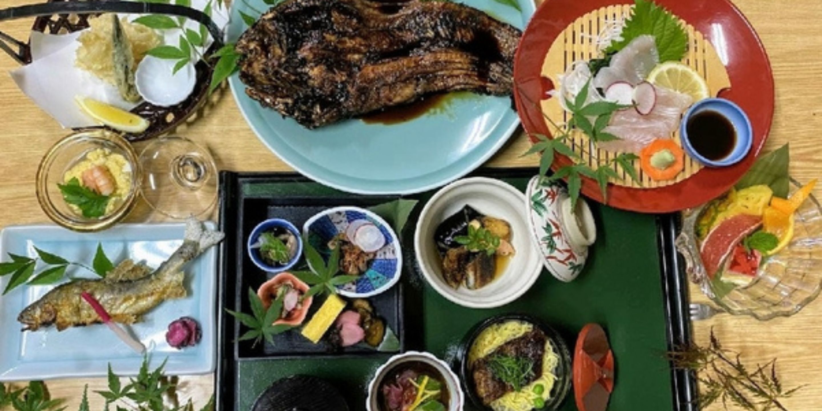 A variety of dishes including grilled fish, sashimi, and other seafood, arranged on a wooden table.