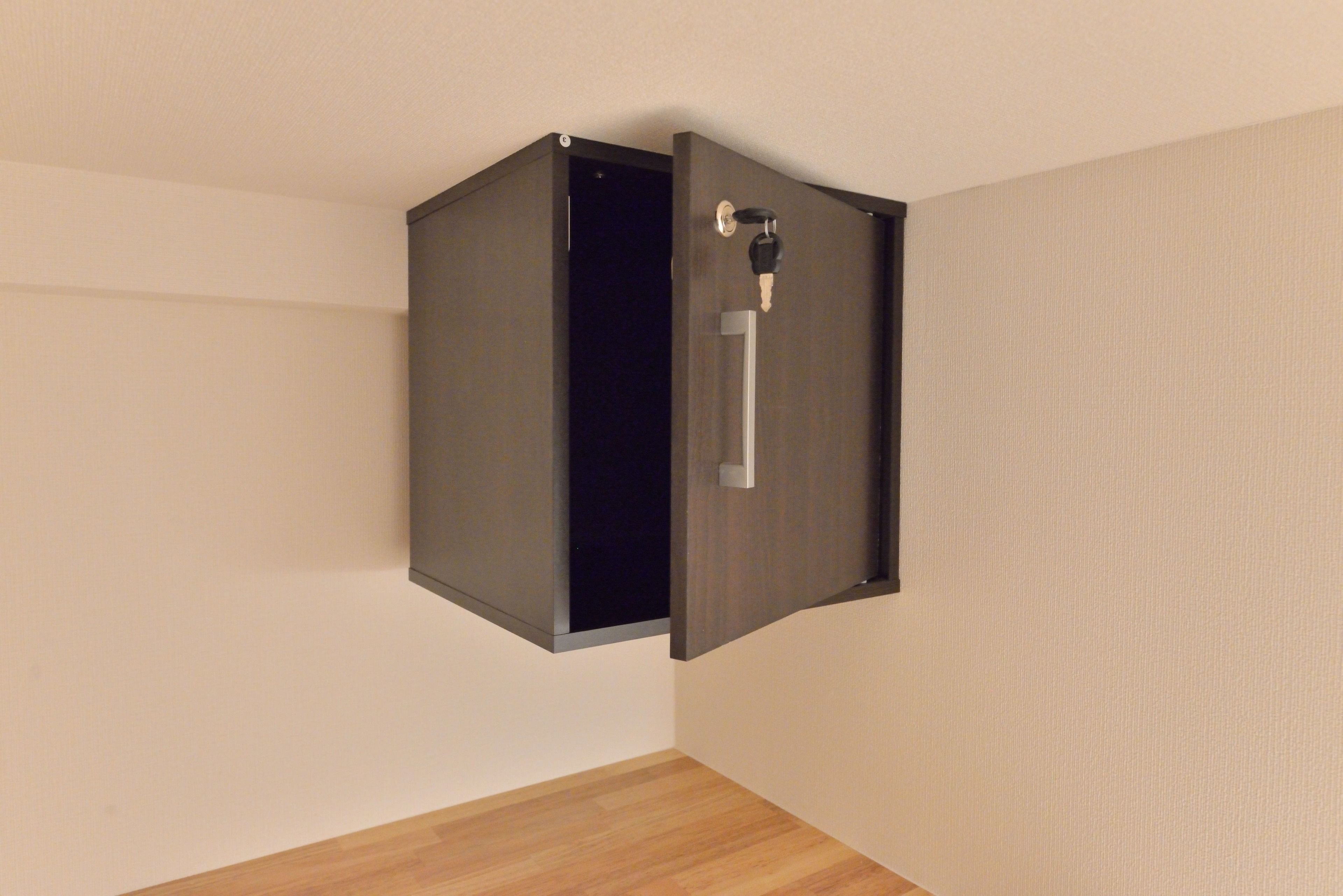 A room with a wooden floor, a wall-mounted cabinet, and a door with a keyhole.