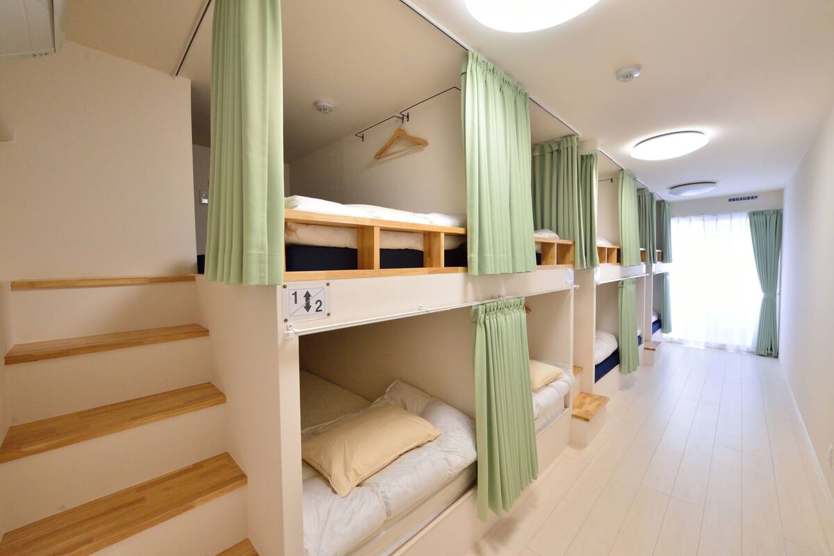Een slaapzaal met stapelbedden, een houten trap en een hangende kapstok.