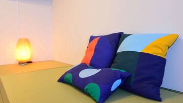 A room with tatami flooring, a wall-mounted TV, and two colorful pillows.