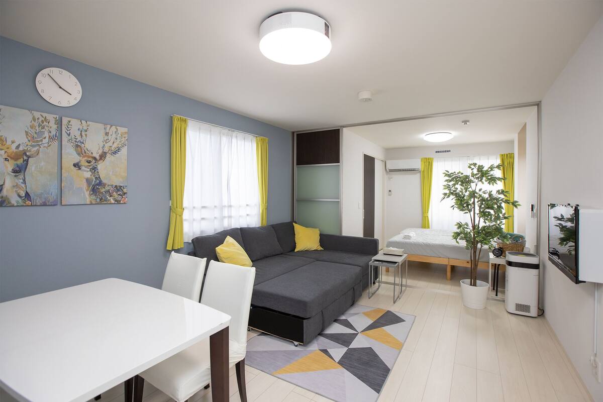 Een moderne woonkamer met een grijze bank, een witte eettafel en gele gordijnen.