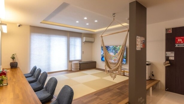 Una habitación moderna con una mesa de madera, varias sillas, una hamaca y un ventanal con persianas.
