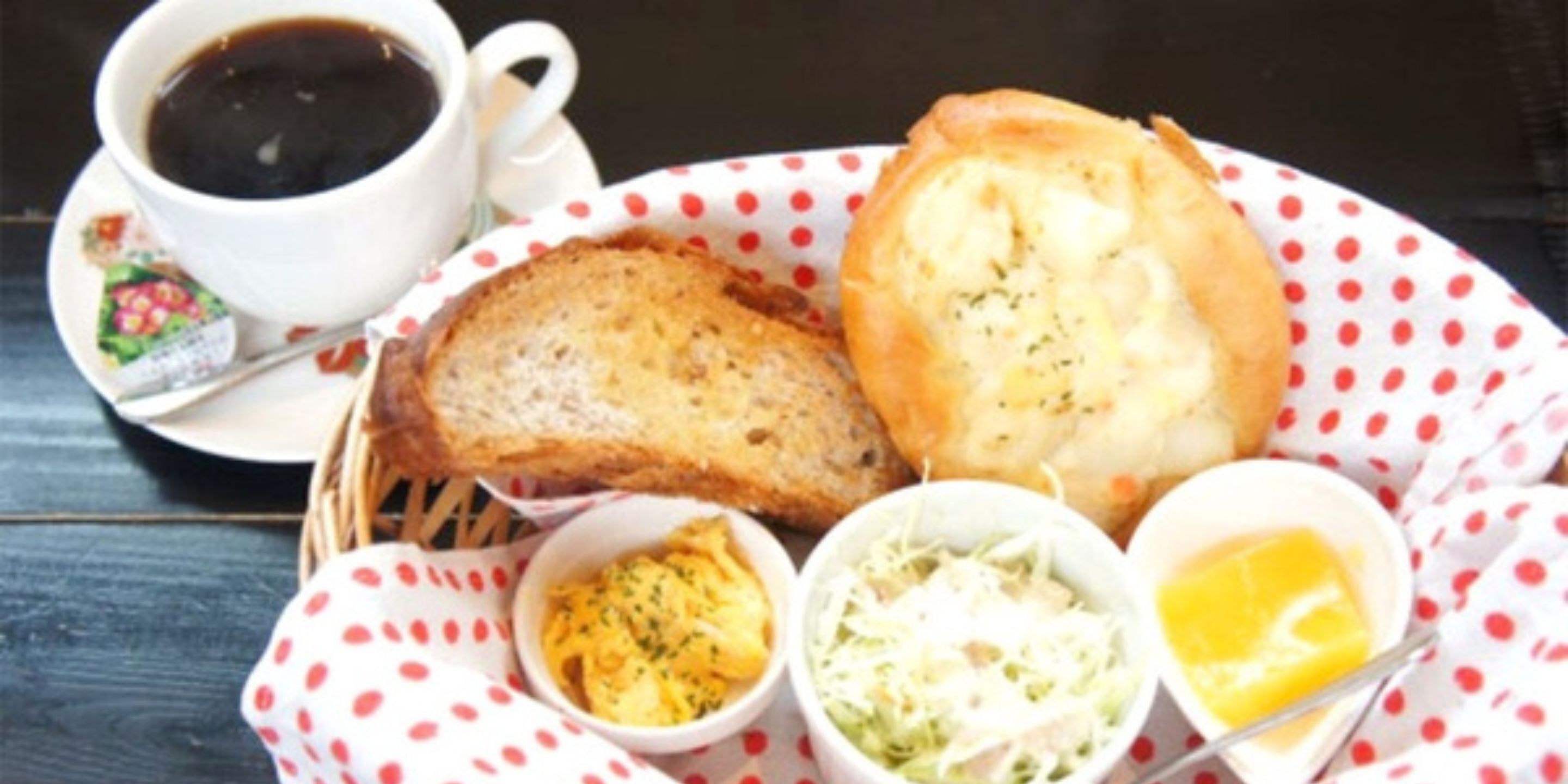 A breakfast tray with toast, a croissant, scrambled eggs, coleslaw, and butter.