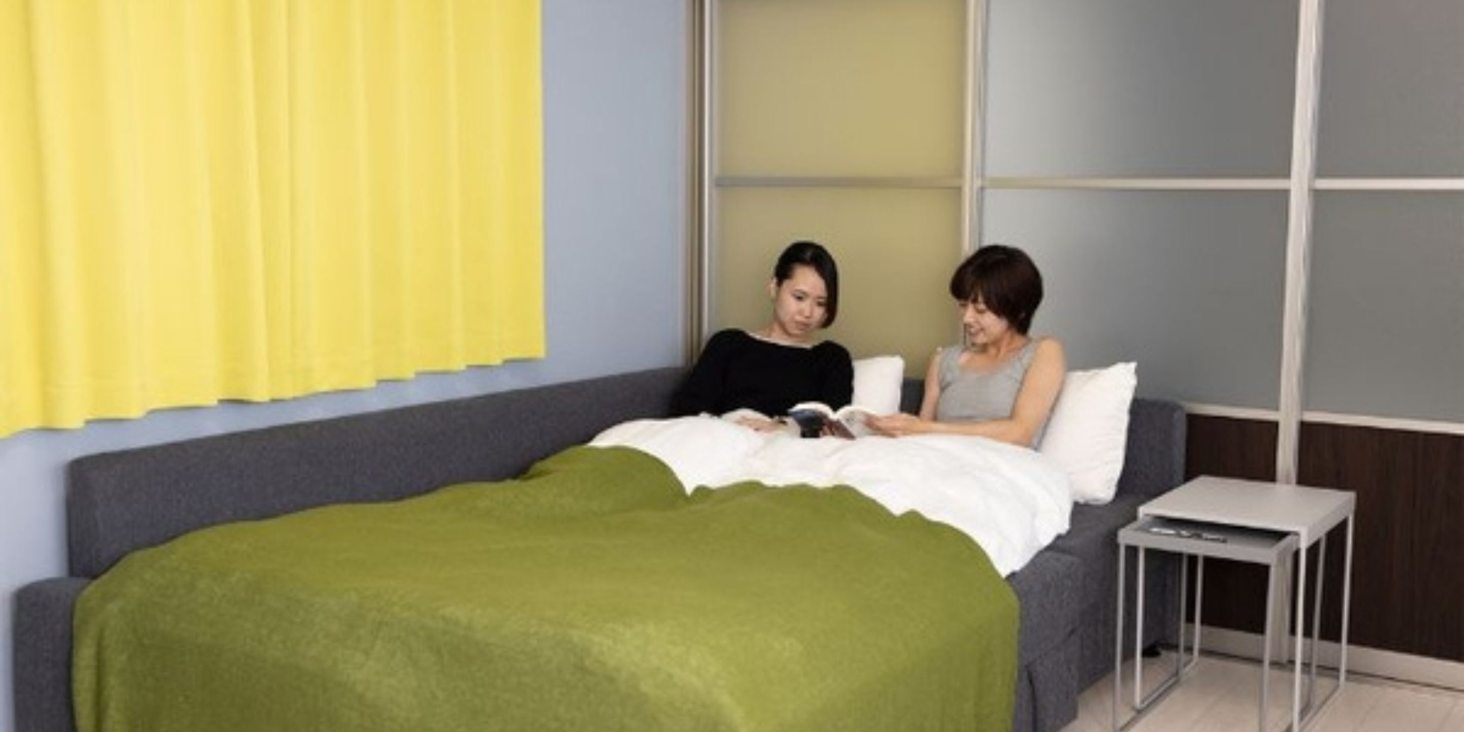 A bedroom with a bed, a bedside table, and a window with yellow curtains.
