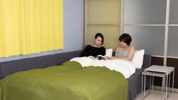 A bedroom with a bed, a bedside table, and a window with yellow curtains.