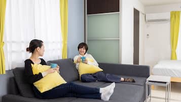 A modern living room with a grey sofa, yellow cushions, a small table, and a bed in the background.