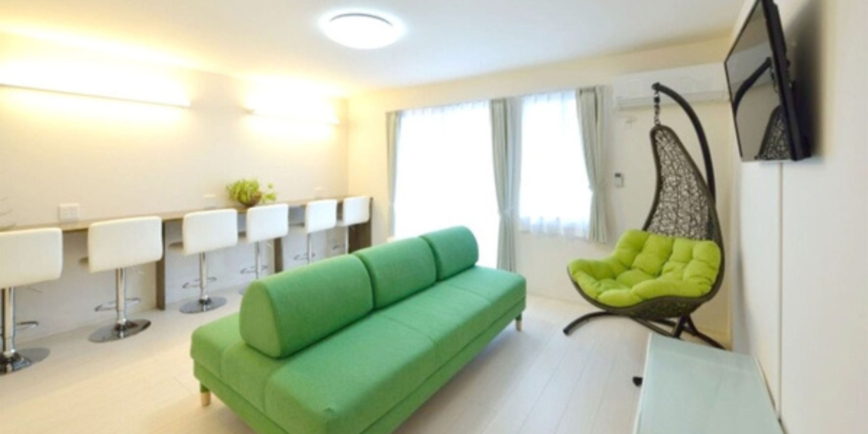 A modern living room with a green sofa, a hanging chair, and a bar area with stools.