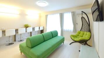 A modern living room with a green sofa, a hanging chair, and a bar area with stools.