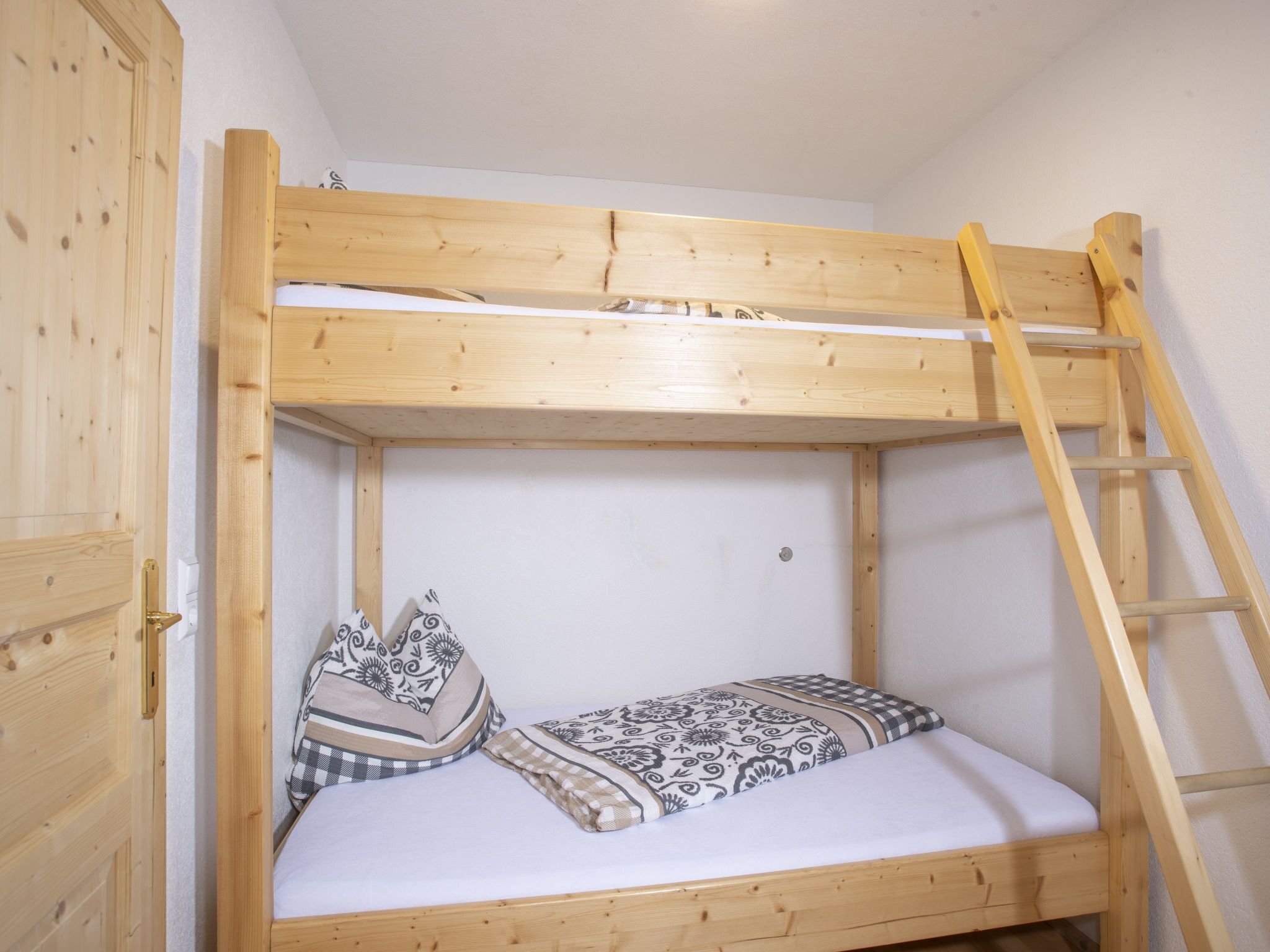 A bunk bed with a ladder, wooden walls, and a white mattress.