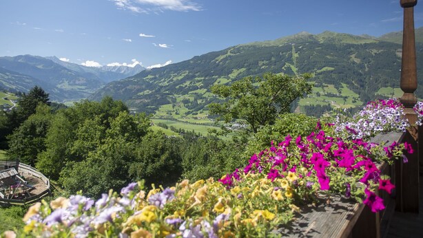 A balcony with a view of a mountainous landscape, a wooden railing, and a flower box with various flowers. - Ferienhof Sonnseitn by Interhome (Kaltenbach)