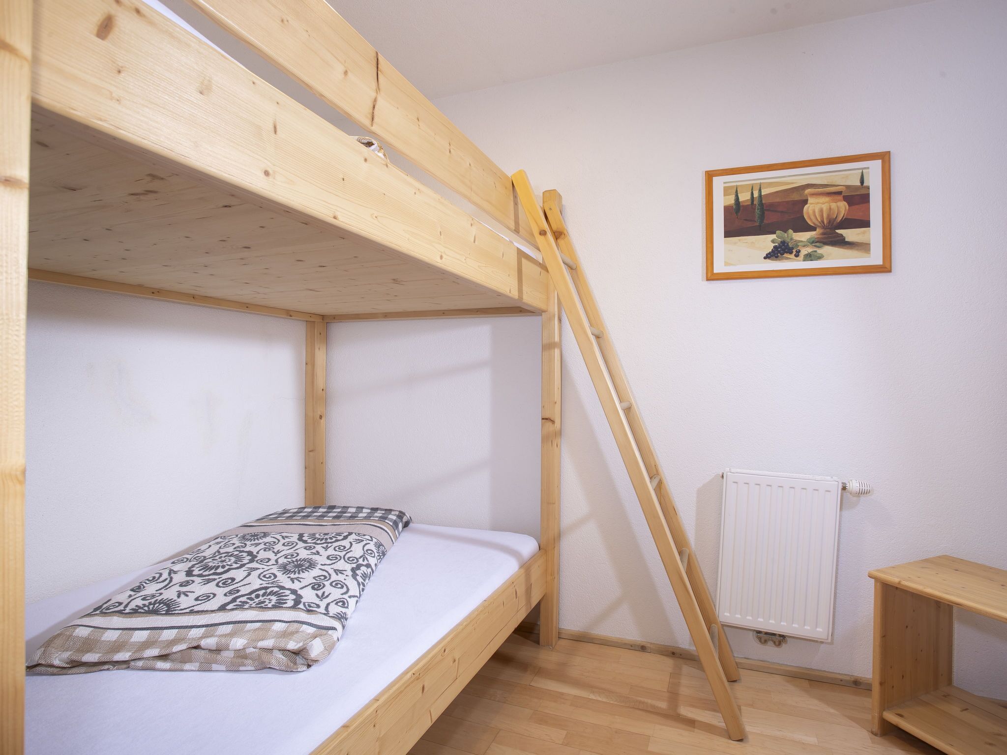 Habitación con literas, una escalera, un radiador y un cuadro en la pared.