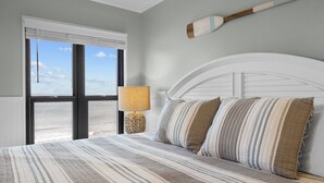 A bedroom with a large bed, a window with blinds, a lamp, and a view of the beach. - Panoramic View DIRECT OCEANFRONT Unit at Summer Winds. Multiple pools, hot tubs (Indian Beach)