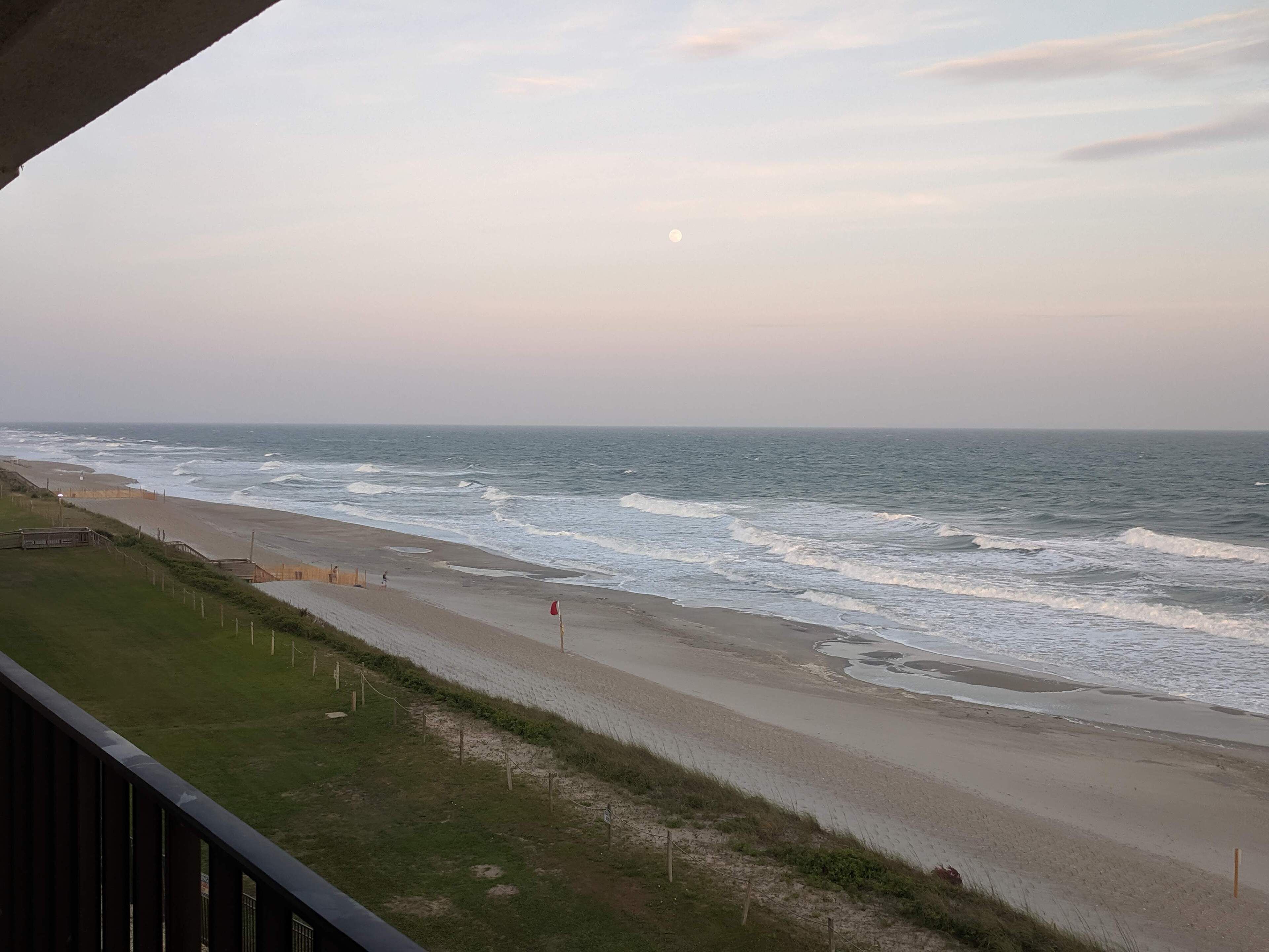 A beach with waves, a fence, and a red flag.