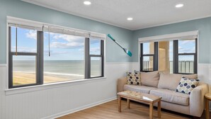 A room with a view of the beach, a sofa, a table, and a paddle leaning against the wall. - Panoramic View DIRECT OCEANFRONT Unit at Summer Winds. Multiple pools, hot tubs (Indian Beach)