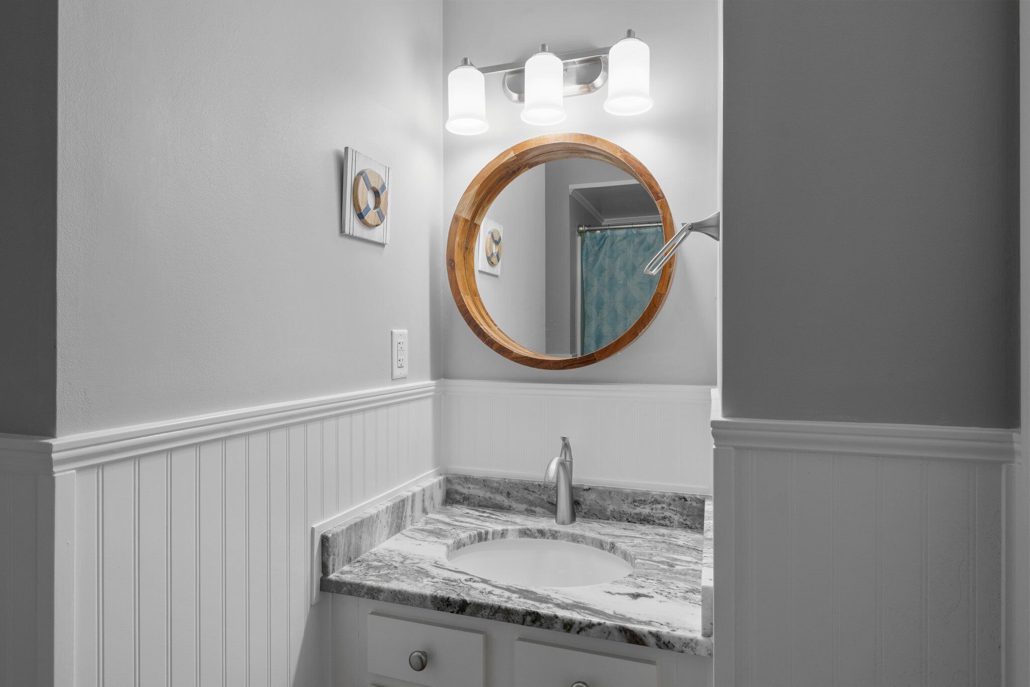 Un baño con un espejo redondo, un lavabo con encimera de mármol y una ducha con cortina azul.