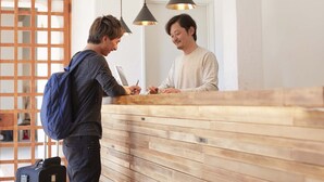 A reception desk with a wooden panel design, a person writing on a notepad, and another person standing beside it. - haku hostel (Shiraoi)