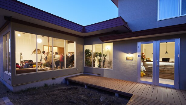 A modern house with large glass windows, a wooden deck, and a visible kitchen area. - haku hostel (Shiraoi)