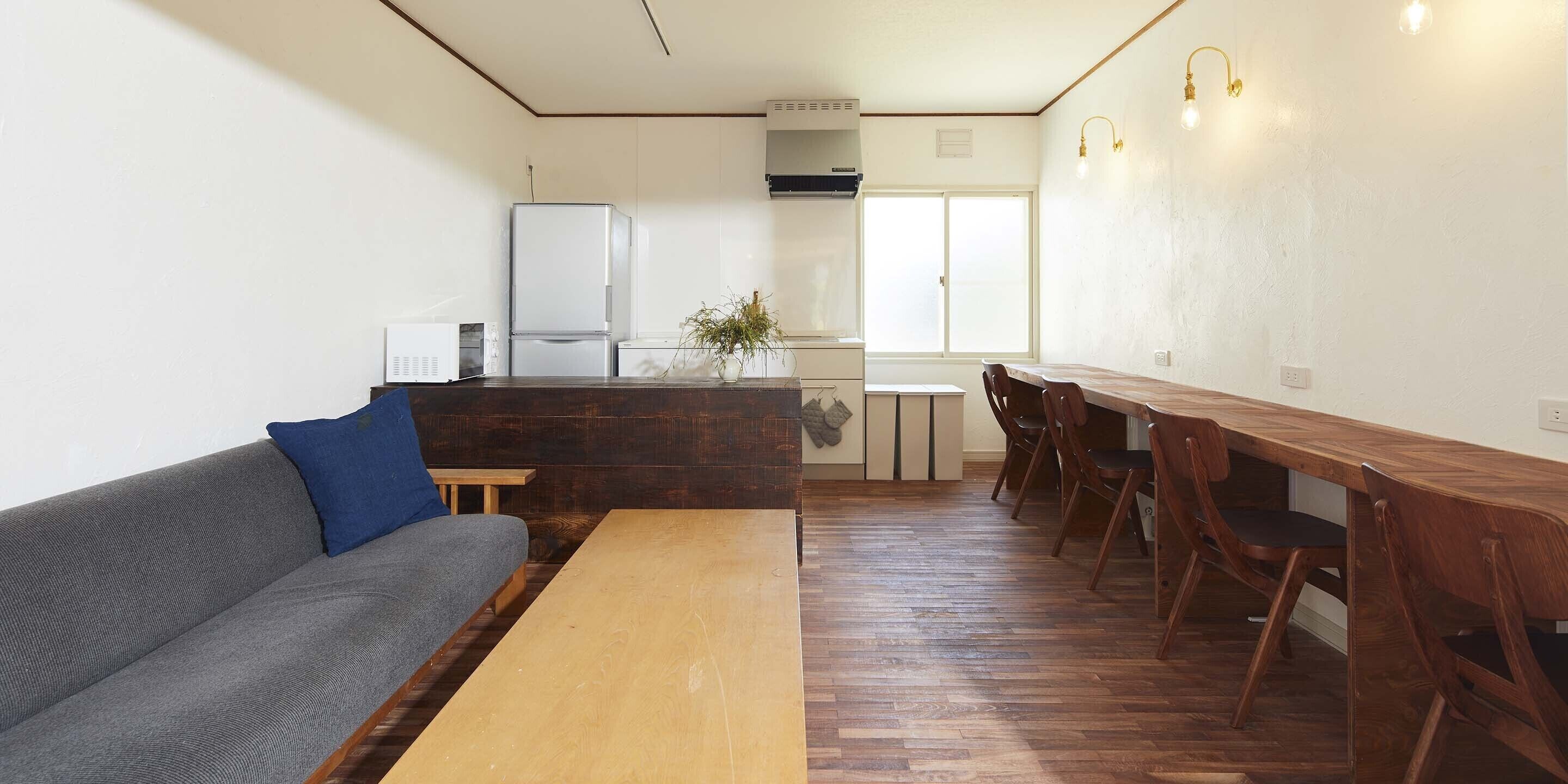 A compact living space with a sofa, a wooden dining table, and a kitchen area with a refrigerator and cabinets.