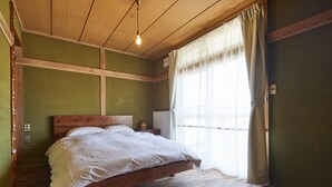 A bedroom with a wooden bed, a single bedside table, a nightstand, and a window with curtains. - haku hostel (Shiraoi)
