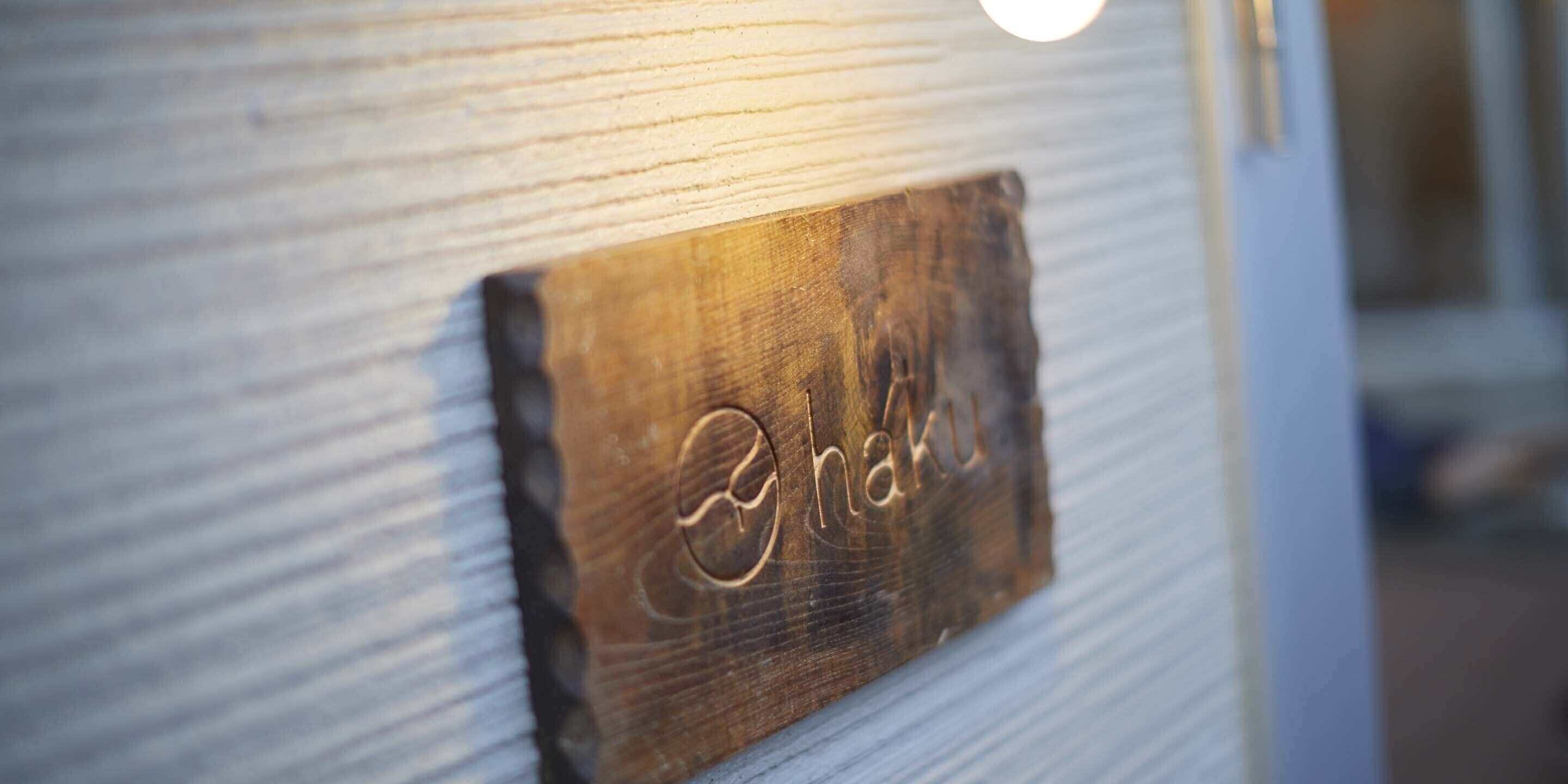 A wooden plaque with the name "Naku" carved into it, attached to a textured wall.