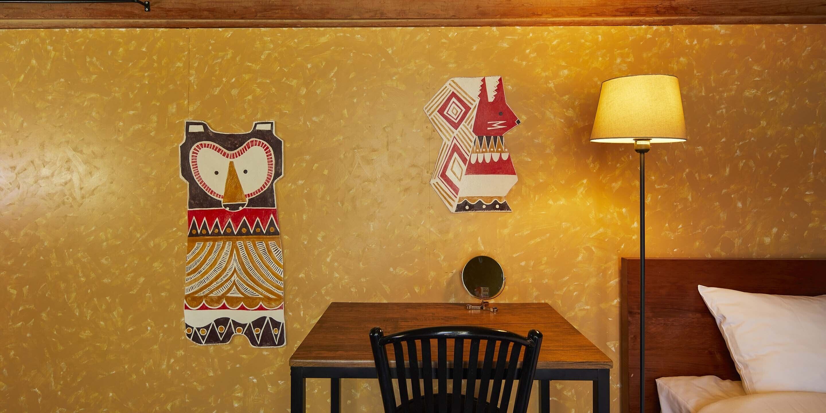 A room with a wooden table, a black chair, a lamp, and two decorative wall art pieces.