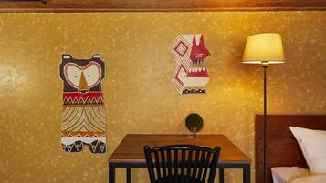 A room with a wooden table, a black chair, a lamp, and two decorative wall art pieces.