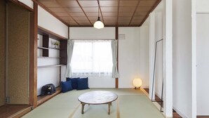 A traditional tatami mat room with a wooden ceiling, a tatami mat table, a shelf with a potted plant, and a sliding door. - haku hostel (Shiraoi)