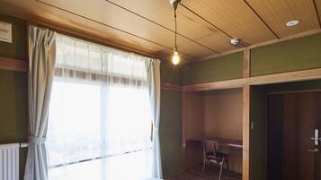 A room with a wooden ceiling, a radiator, a window with curtains, a desk, and a chair.