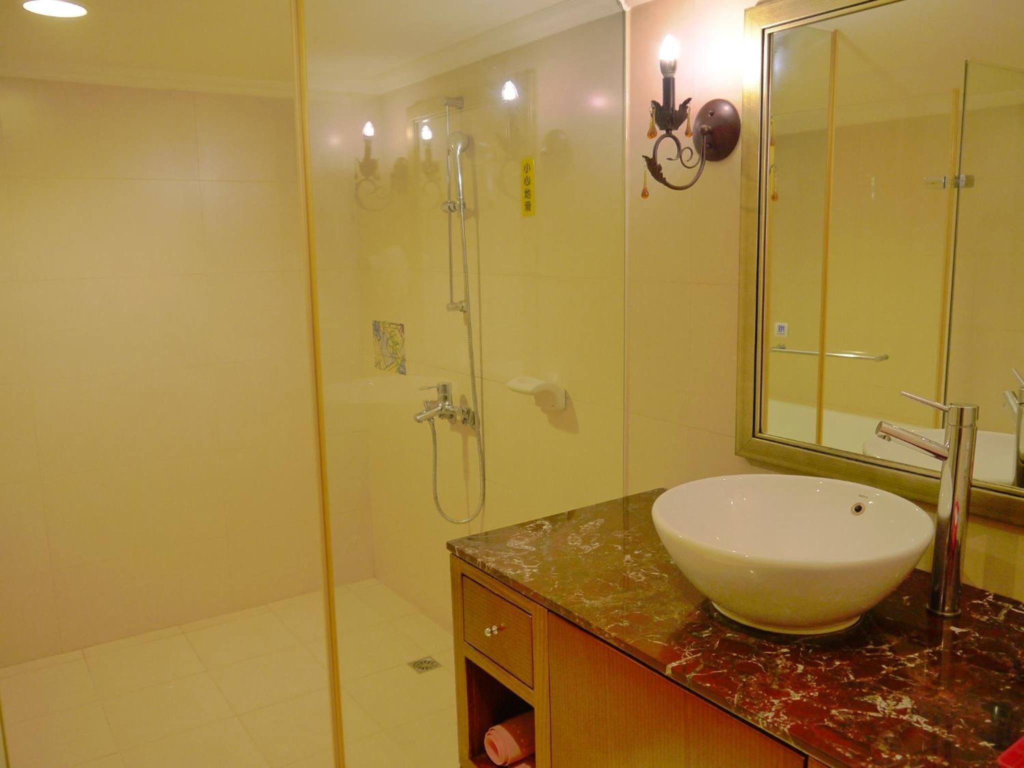 A bathroom with a glass-enclosed shower, a marble countertop, a white sink, and a mirror.