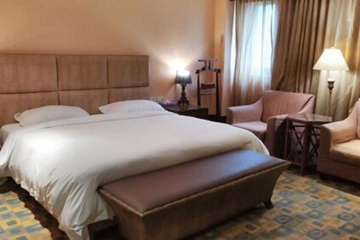 A hotel room with a large bed, a small table, a chair, and a sofa.
