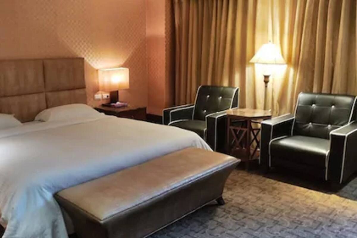 Une chambre d’hôtel avec un grand lit, deux chaises, une petite table et une lampe.