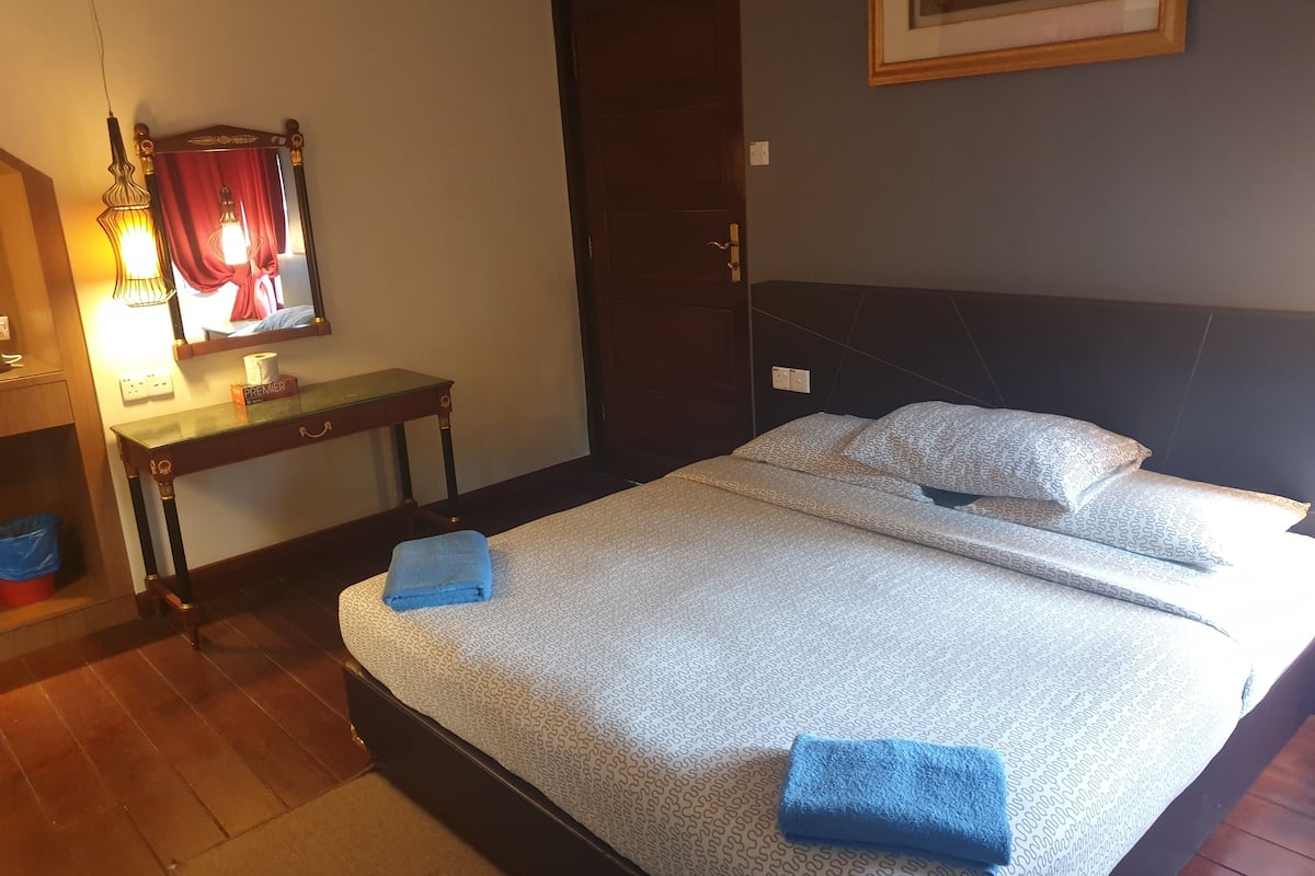 A hotel room with a bed, a bedside table with a lamp, a mirror, and a framed picture on the wall.