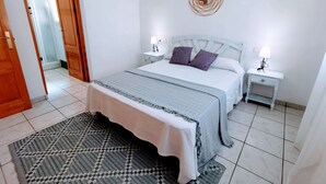 A bedroom with a bed, two bedside tables, a nightstand, a patterned rug, and a door leading to another room. - 0302 Villa Monte Verde Pera (Javea / Xàbia)