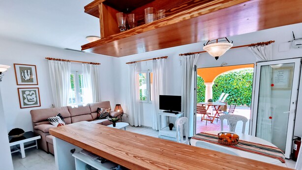 A modern living room with a wooden bar, a sofa, a TV, and a dining area with a table and chairs. - 0314 Villa Monte Verde Cereza (Javea / Xàbia)